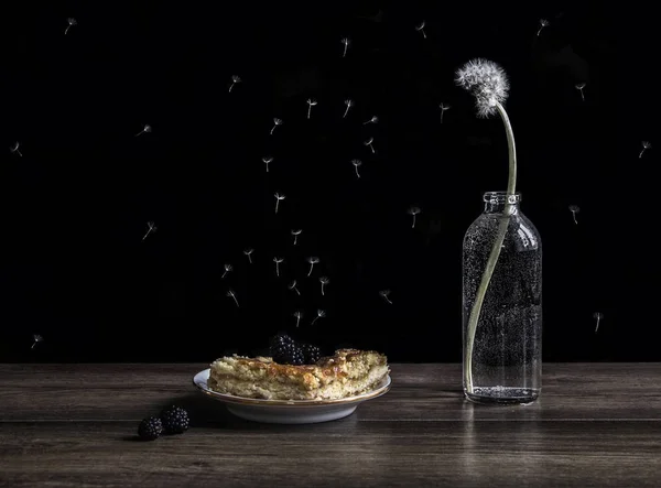 Diente de león en un jarrón en una mesa y un pastel en un plato con un cuento de hadas de mora la magia de una mosca pelusa — Foto de Stock
