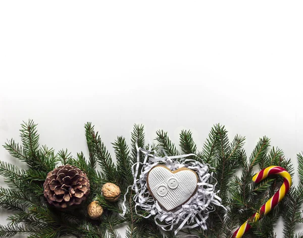 На белом фоне на еловых ветвях, лежащих на рождественском конусе из орехов и леденец с карамелью — стоковое фото