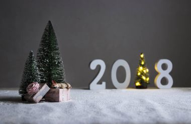 karla kaplı bir alanda köknar ağaçlarının altında belgili tanımlık köpek hediyeler uyuyor ve Uzaktan 2018 nerede bir Noel ağacı ışıkları ile rolü rakamlar