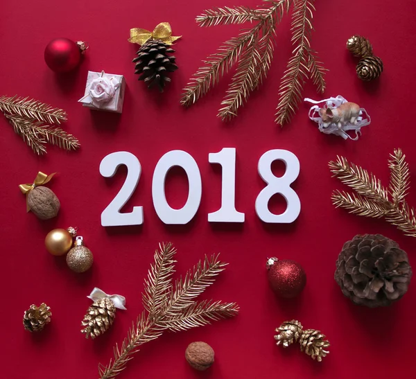Sur fond de framboise rouge, les décorations du Nouvel An et de Noël et les branches d'or d'épinette sont disposées en cercle et au centre se trouvent des figures blanches 2018 — Photo