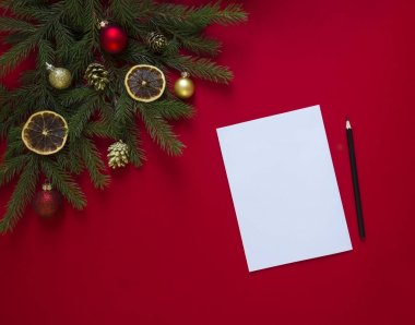 kırmızı bir arka plan üzerinde yeşil çam dalları Noel gingerbread, altın koniler, portakal ve topları ile dekore edilmiş ve üzerinde beyaz bir levha ve siyah kalem tarafı 