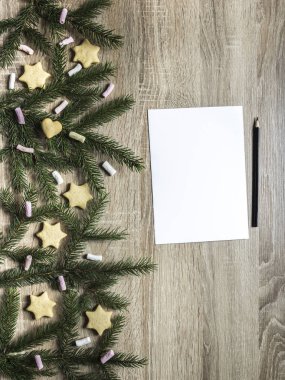 Beyaz bir levha kağıt ve ahşap bir masa üzerinde sağ yanındaki siyah kalem yalan olan çam dalları ve marshmallow, Kızıl Yıldız ve bir kalp şeklinde bisküvi 