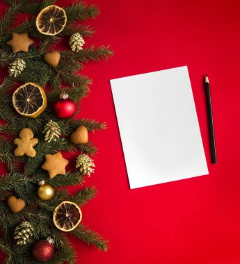 kırmızı bir arka plan üzerinde yeşil çam dalları Noel gingerbread, altın koniler, portakal ve topları ile dekore edilmiş ve üzerinde beyaz bir levha ve siyah kalem tarafı 