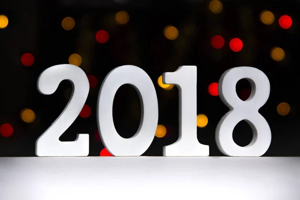 Chiffres 2018 debout sur une table blanche sur un fond de lumières bokeh jaune et rouge — Photo
