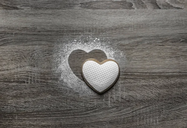 Op een houten achtergrond met gemalen poeder sneeuw een silhouet van het hart wordt gegoten en hieronder op de silhouet ligt een cookie in de vorm van een hart — Stockfoto