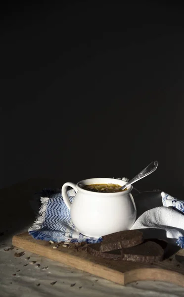 På tabell blå servett med prydnad mönster och soppa terrin med gul soppa på solen bröd träskiva frön mörk bakgrund — Stockfoto