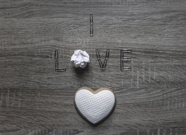 Op een houten achtergrond ligt het paperclip woord liefde in plaats van de letter o papier klonterige verfrommeld cookie hart met mastiek — Stockfoto