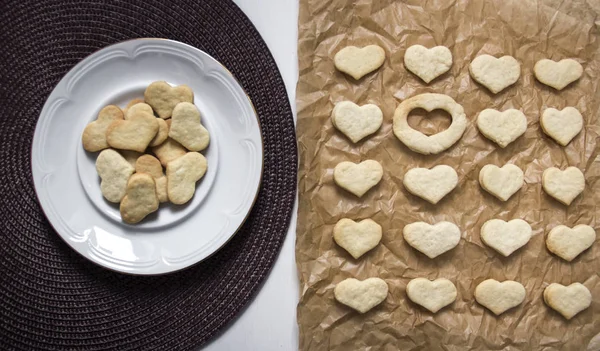 Witte achtergrond donker servet plaat met cookies in het hart van de vorm bakken papier ligt een cookie in vorm hart en één plaats is leeg — Stockfoto