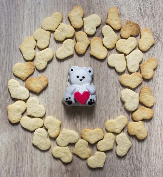 wooden background circle lie gingerbread cookies shape of a heart center lies cake in the shape of a bear with a heart his hands