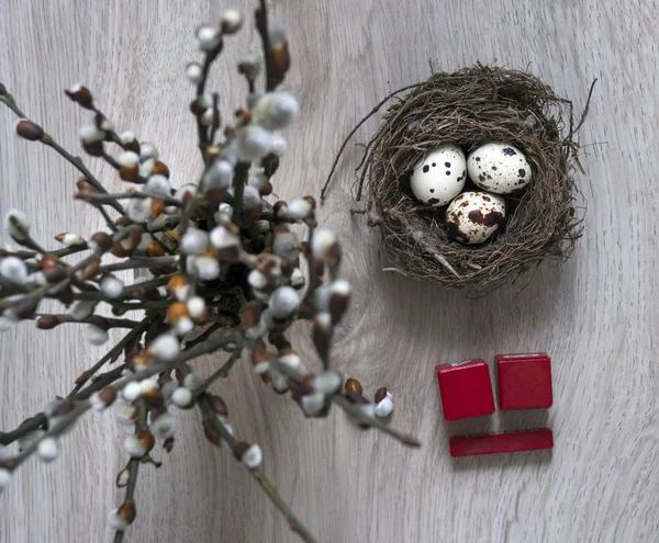 On a wooden table lies a nest with eggs and stands a vase with willow branches calendar Easter cubes April — Stock Photo, Image