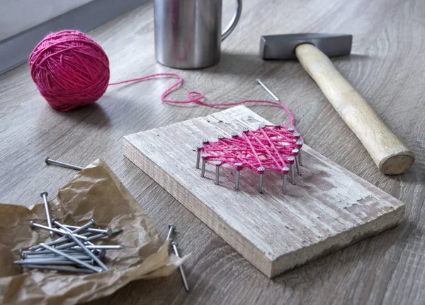 on a wooden table lies a hammer of a nail of a thread pink and a gift with your hands  heart of threads and nails a cup of coffee
