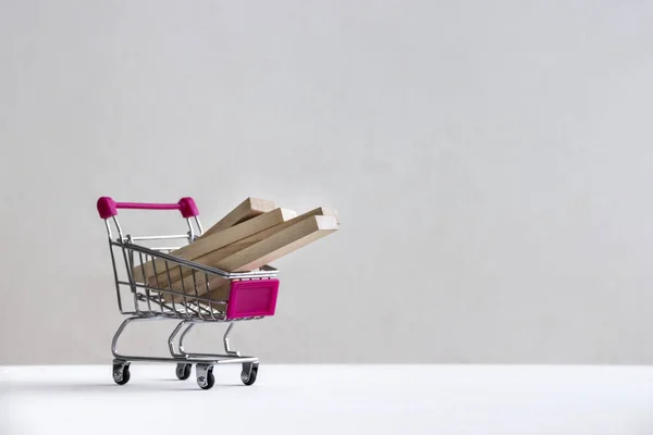 Em um soalho branco em um fundo branco há um carrinho de compras com blocos de madeira de conselhos — Fotografia de Stock