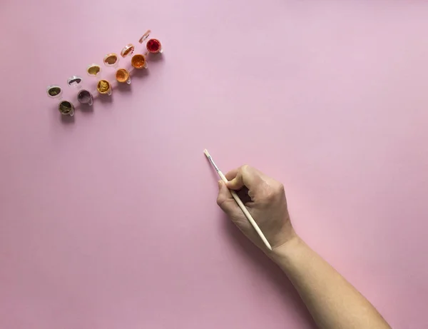 Bir boya fırçası ile kırmızı ve turuncu renk pembe bir arka plan üzerinde el berabere boyalar — Stok fotoğraf