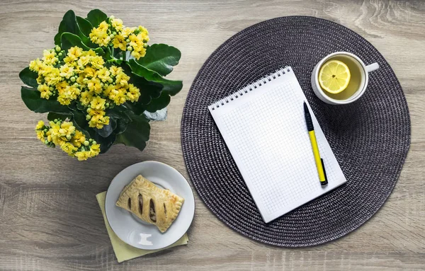 Sur un fond en bois une fleur de couleur jaune kalandive serviette ronde tasse de thé en osier citron soucoupe croissant petit déjeuner — Photo