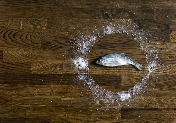Sobre un fondo de madera de pequeños discos marrones oscuros círculo plato sal marina pimienta condimentos cilantro vertido en el centro pescado salado seco — Foto de Stock