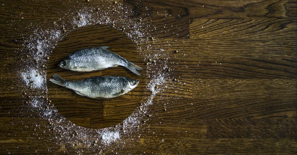 Sobre un fondo de madera de pequeños discos marrones oscuros círculo plato sal marina pimienta condimento cilantro vertido vapor dos pescados secos salados — Foto de Stock