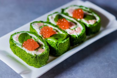 Süzme peynirli ıspanaklı bisküvi rulosu, gri bir masada beyaz dikdörtgen bir tabakta tuzlu somon ve kırmızı havyar. Yumuşak odak.