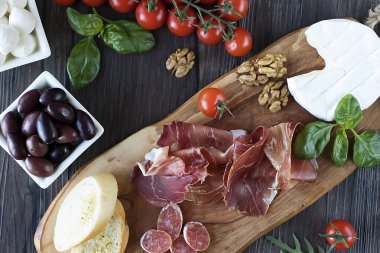 Prosciutto, ekmek, zeytin, ceviz, mozzarella, salam, fesleğen ve kiraz domatesleri kahverengi ahşap tahtada. Akdeniz mutfağı. Üst görünüm