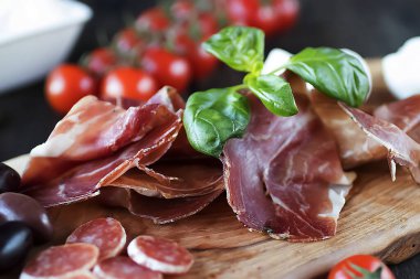 Prosciutto, ekmek, zeytin, ceviz, mozzarella, salam, fesleğen ve kiraz domatesleri kahverengi ahşap tahtada. Akdeniz mutfağı.