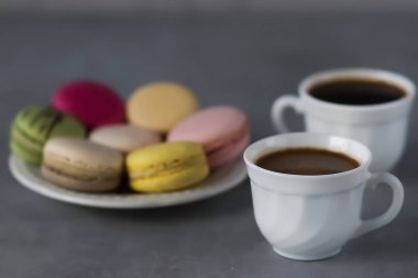 Beyaz tabakta çeşitli kurabiyeler ve gri arka planda iki beyaz fincan kahve. Yumuşak odak.