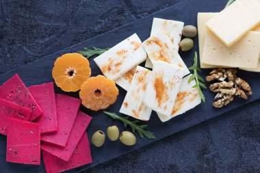 Siyah tahta üzerinde çeşitli peynirler, zeytin, ceviz ve meyveler. Yakın plan. Yumuşak odak.