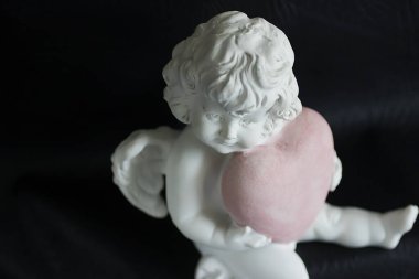 Siyah arka planda pembe kalpli beyaz bir melek. Yumuşak odak.