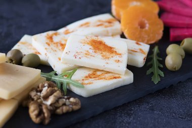 Siyah tahta üzerinde çeşitli peynirler, zeytin, ceviz ve meyveler. Yumuşak odak.