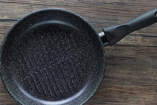 Black frying pan on brown wooden background. Top view.