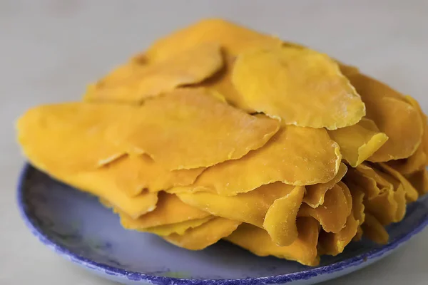 Sun-dried mango slices on a blue plate close-up. Soft focus.
