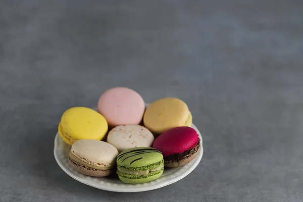 Assorted macaroon cakes in a white plate on a gray background. Soft focus.