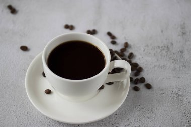 Beton arka planda siyah kahve ve kahve çekirdekleri olan beyaz bir fincan. Yumuşak odak.
