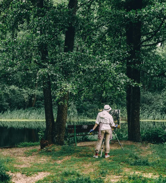 Kvinnliga artist på stranden av floden ritar en bild. Natur, träd koncept — Stockfoto