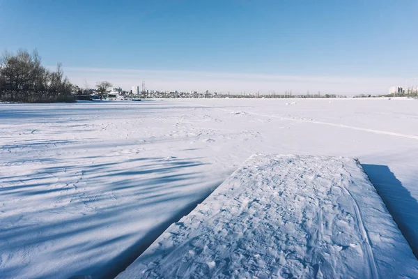 Molo v sníh a zamrzlé jezero ve sněhu. Slunný zimní den ve městě — Stock fotografie