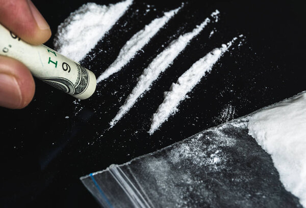 Hand of man holds rolled banknote for snorting cocaine powder. Problems with dru