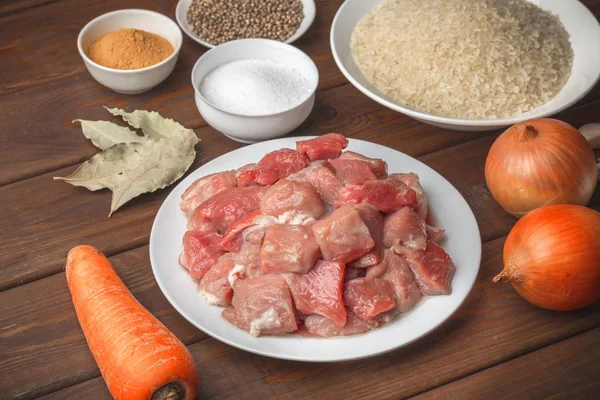 Cocinar ingredientes. Carne cruda en rodajas, arroz, especias, ajo, zanahoria, cebolla, laurel — Foto de Stock