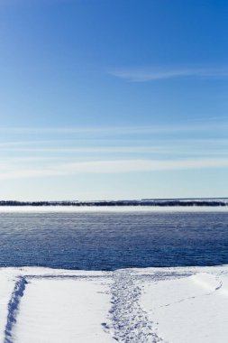 Göl kışın donmuş değil. Buhar suyun üstünde yükselir. Parlak mavi gökyüzü.