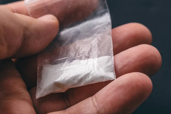 Рука мужчины держит на ладони пластиковый пакет с кокаином порошок или другой препарат . — стоковое фото