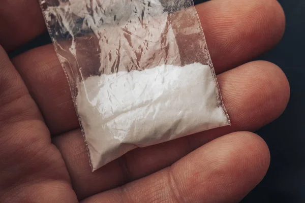 Пластиковая упаковка с кокаиновым порошком или другими наркотиками в руках человека. Макро крупным планом — стоковое фото