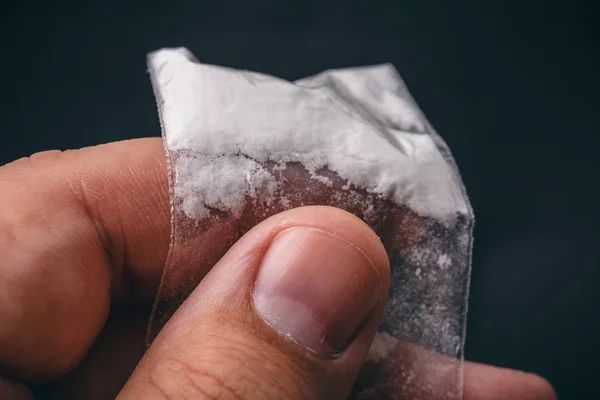 Mans mão contém pacote de plástico com pó de cocaína ou outra droga. Macro foto — Fotografia de Stock