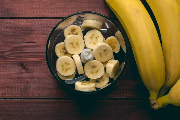 Нарезать куски банана в блендере и бананы на темном деревенском деревянном столе — стоковое фото