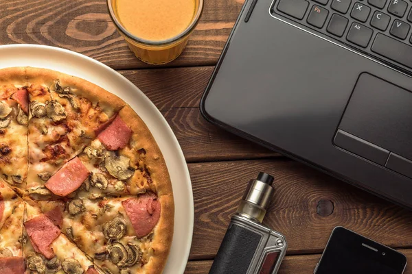 Pizza with ham and mushrooms on a plate, laptop, electronic cigarette or vape