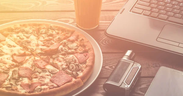 Pizza with ham and mushrooms on a plate, laptop, electronic cigarette or vape