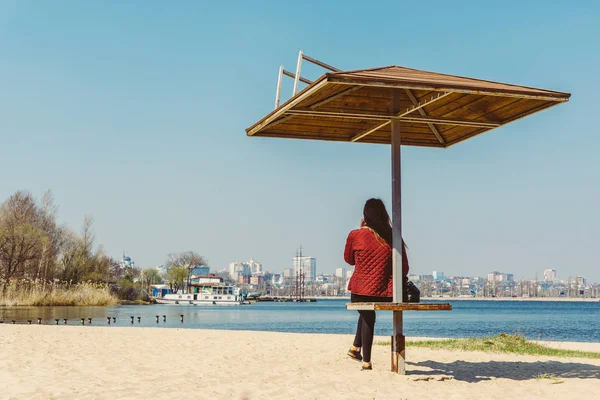 暖かい春の日の湖のビーチに木製の傘の下で座っている女の子 — ストック写真