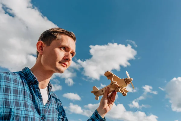 Мечтатель, молодой человек держит в руке деревянный игрушечный самолет на голубом фоне неба с копировальным пространством — стоковое фото