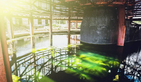 Water reservoir with green water of abandoned cooling tower in sun light
