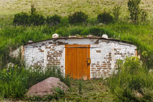 Dugout com uma porta de madeira em uma colina com grama verde na localidade de um agricultor rural — Fotografia de Stock