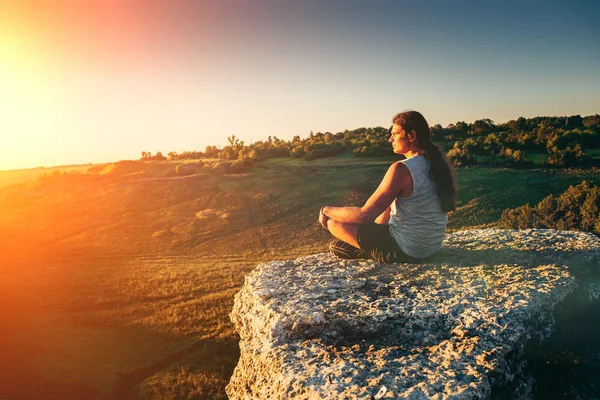 Gün batımı ışınları uçurumun kenarında uzun saçlı genç hipster derin derin düşünür