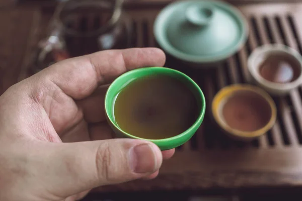 Mão masculina segurando piala ou tigela com Shu Puerh no fundo turvo do conjunto de chá asiático — Fotografia de Stock
