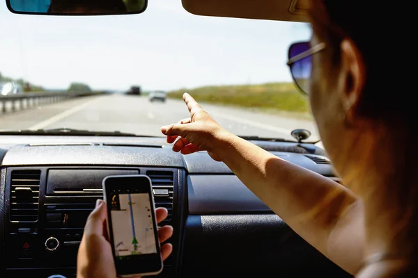 Perjalanan dalam konsep mobil, gadis menunjukkan smartphone di tangannya dengan aplikasi navigasi gps terbuka — Stok Foto