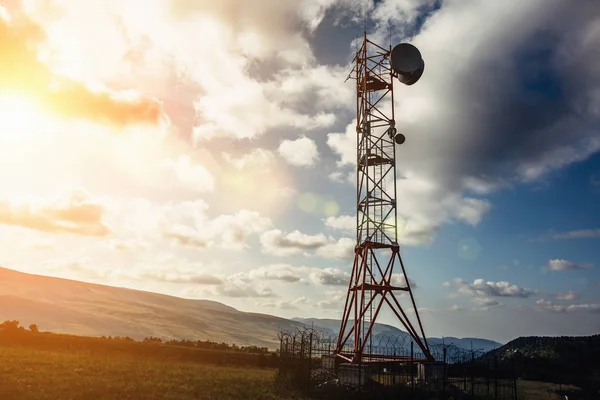 Torre de telecomunicações com antena de prato e móvel em montanhas ao pôr-do-sol céu fundo — Fotografia de Stock